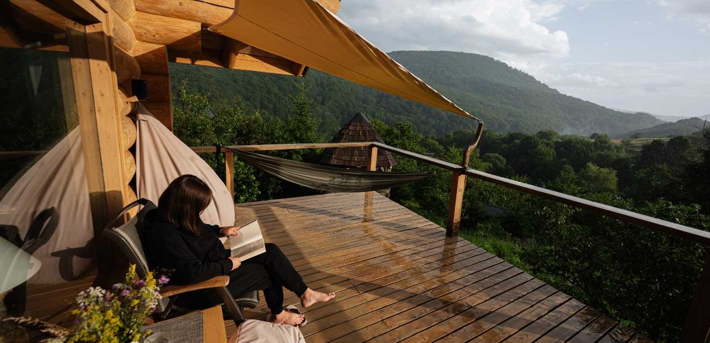 a woman on a reading retreat overlooking wilderness from a cabin