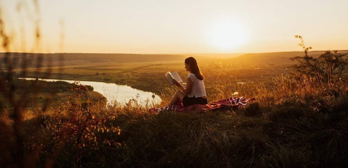 woman reading overlooking a river at sunset