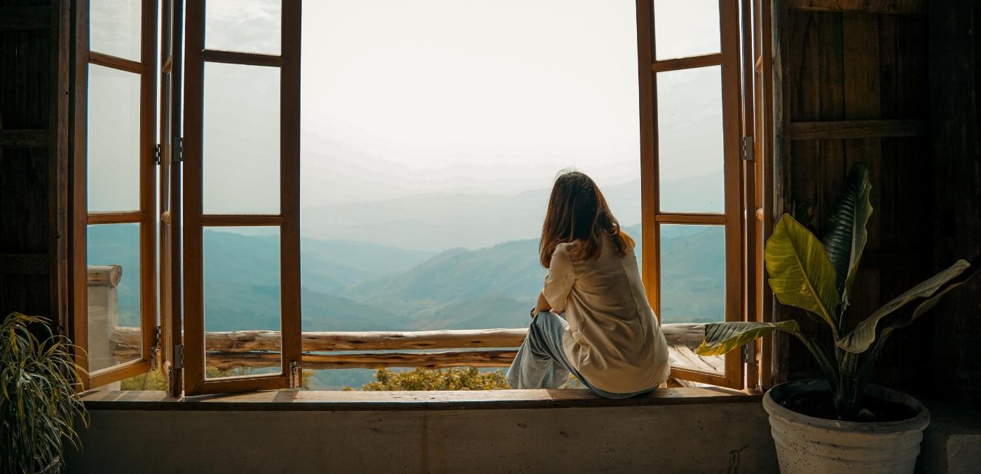 woman sitting on windowsill overlooking mountains